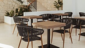 Un interior moderno con pared de piedra, una escalera de madera y un comedor con sillas negras y mesas de madera.