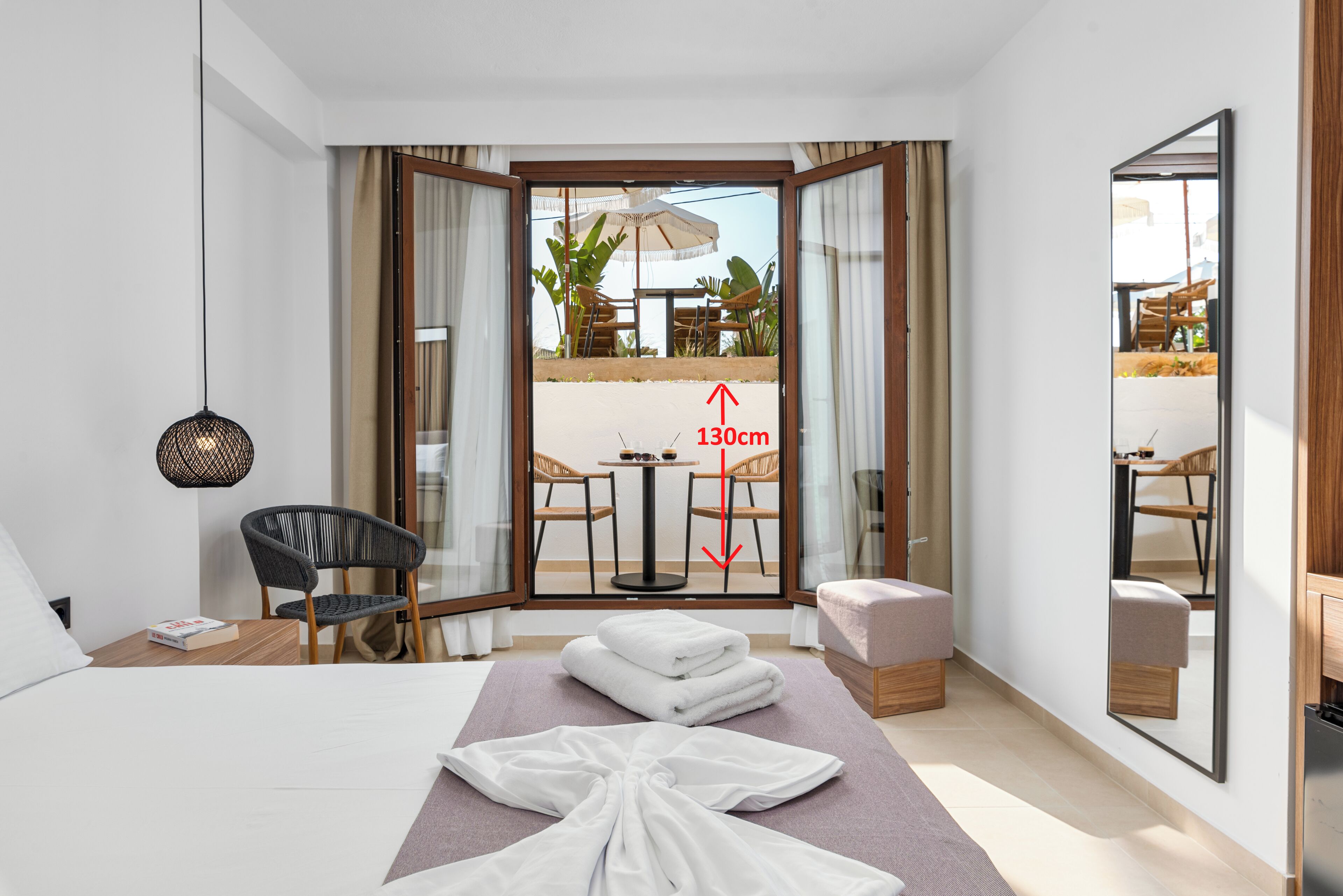 A hotel room with a bed, a chair, a table with an umbrella, and a view of an outdoor area.