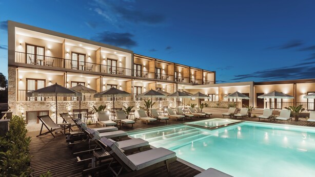 Un hotel de varios pisos con piscina, asientos al aire libre y balcones bien iluminados.