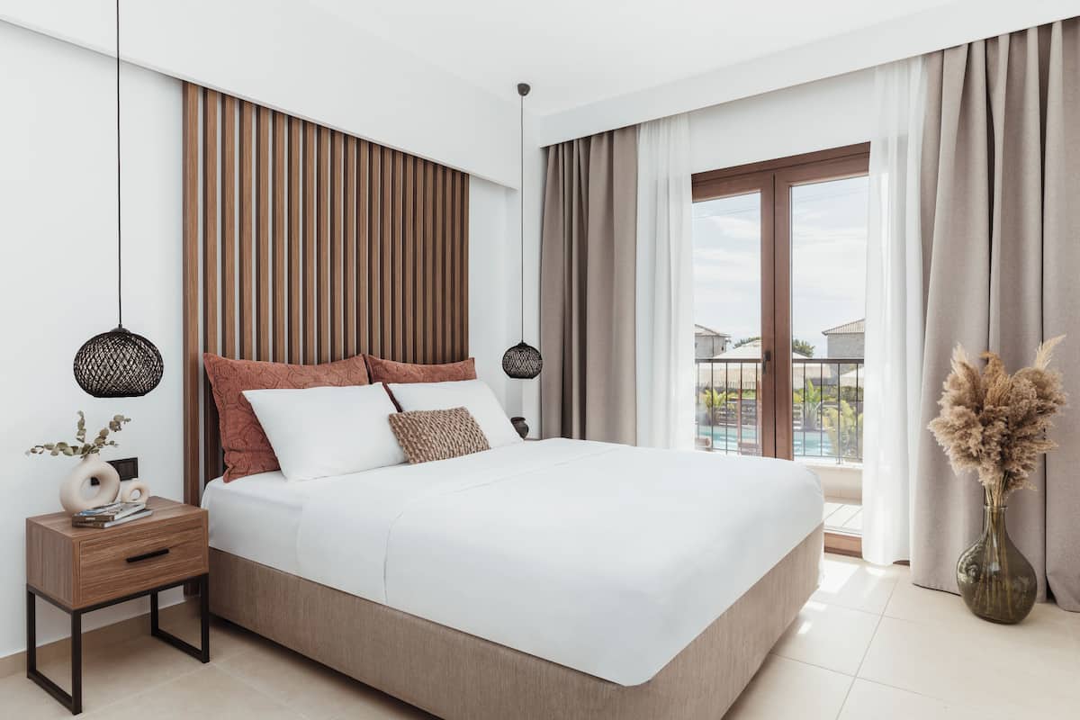 Un dormitorio moderno con una cama grande, una mesita de noche, un jarrón con flores secas y vistas al exterior a través de un amplio ventanal.