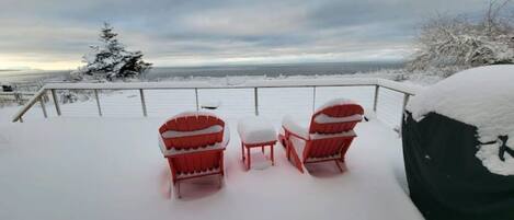 Um alpendre coberto de neve com duas cadeiras Adirondack vermelhas e uma pequena mesa.