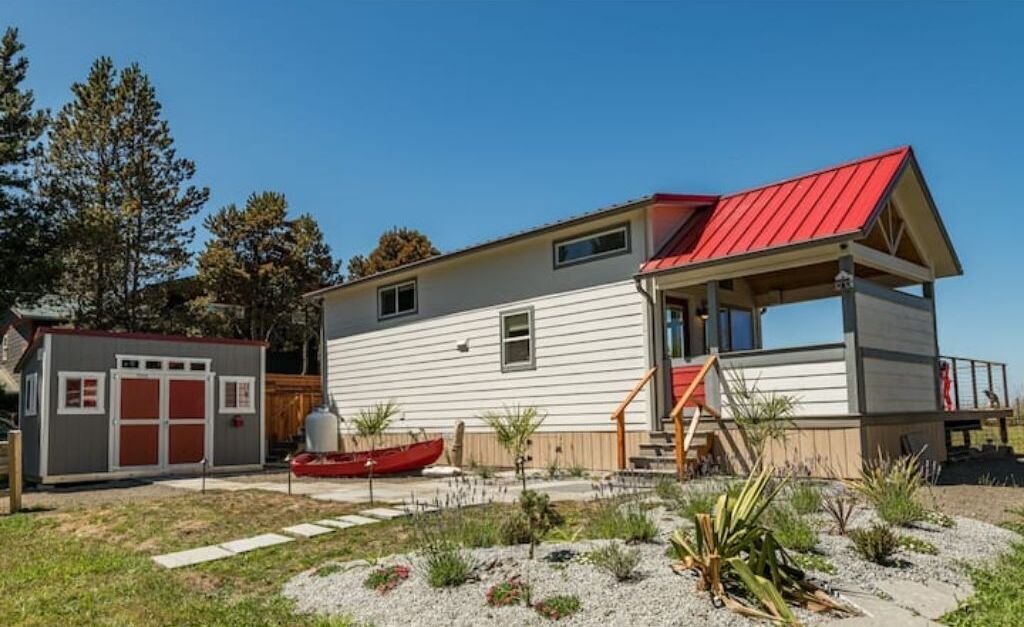 Een tweelaags huis met een rood dak, een klein terras en een boot in de voortuin.