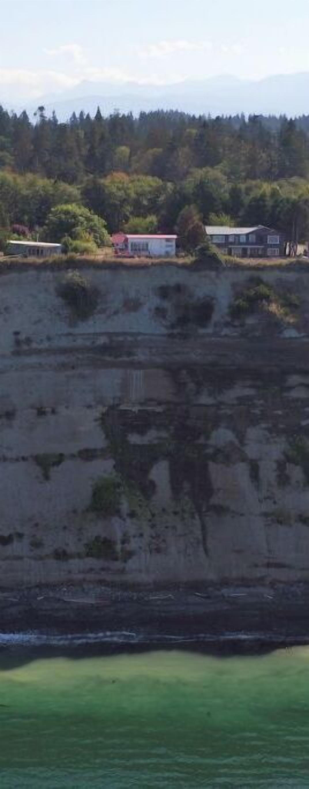 A coastal cliff with buildings on top, overlooking a body of water.