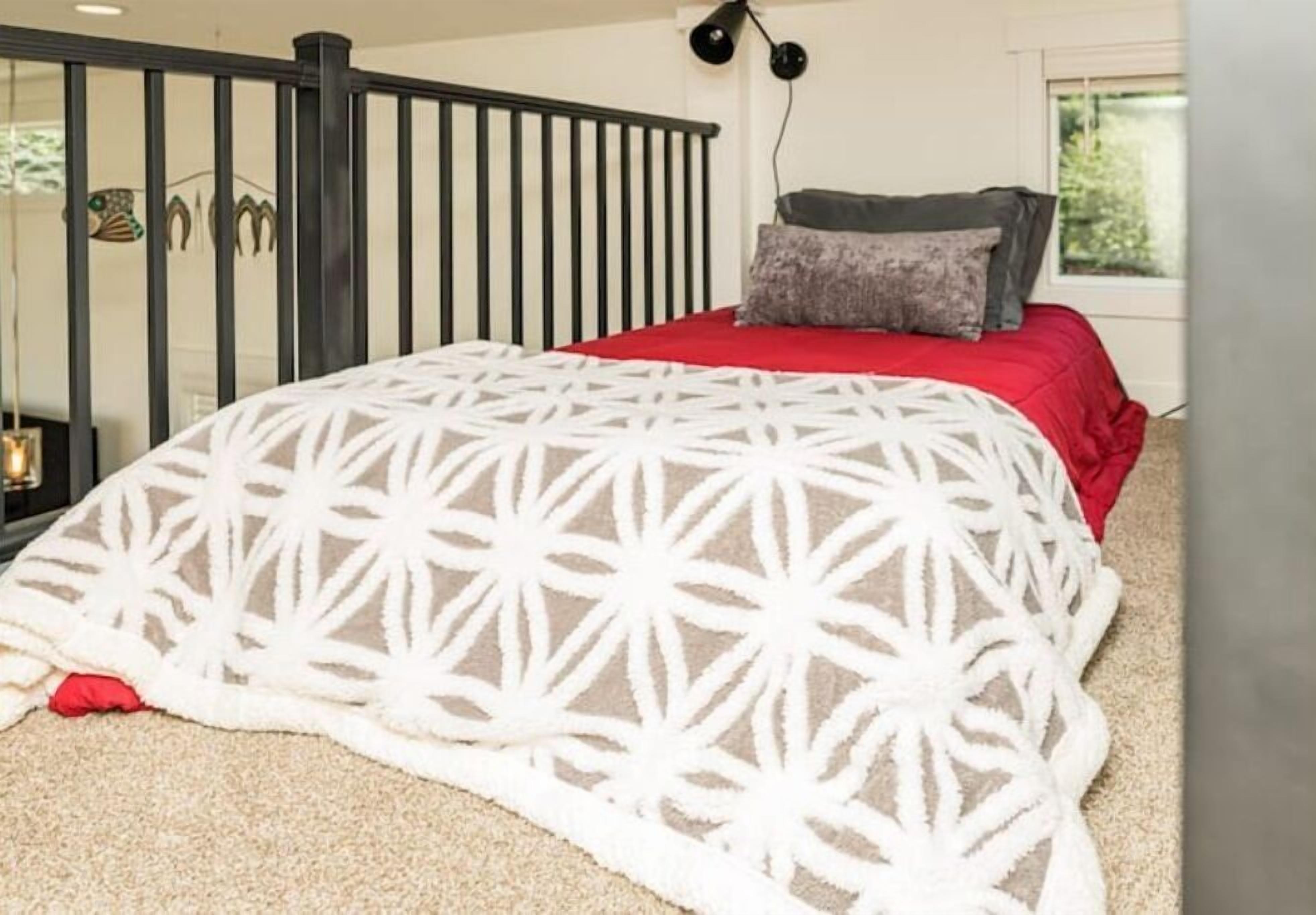 A bedroom with a bed, a red and white patterned blanket, a grey pillow, a black headboard, and a window with a view of greenery.