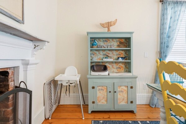 A room with a white fireplace, a blue cabinet with a world map design, a white baby high chair, and a yellow chair. - Historic Home, Walk to Seaport & Downtown (Stonington)