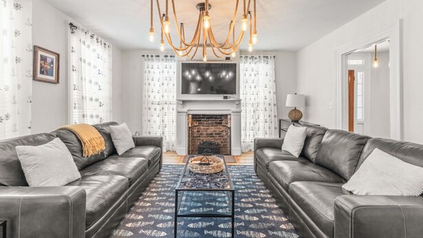 A modern living room with two leather sofas, a patterned rug, a fireplace, and a chandelier.