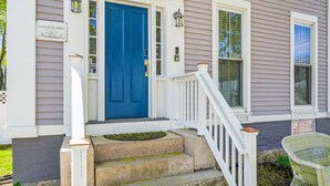 A house with a blue front door, white porch railing, and a small outdoor chair.