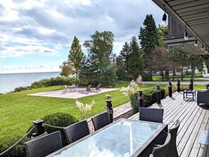 En terrass med utemöbler och utsikt över en vackert anlagd trädgård och en vattenyta.