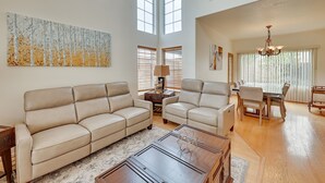 A spacious living room with a high ceiling, a large abstract painting, a dining area with a chandelier, and a staircase leading to an upper level. - Lake Elsinore Vacation Rental ~ 4 Mi to the Lake! (Lake Elsinore)