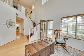 A spacious room with a wooden staircase, a large window with blinds, a rocking chair, and a decorative mirror. - Lake Elsinore Vacation Rental ~ 4 Mi to the Lake! (Lake Elsinore)
