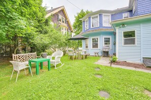 Un jardin avec une table et des chaises vertes, une chaise berçante blanche et un petit coin barbecue.