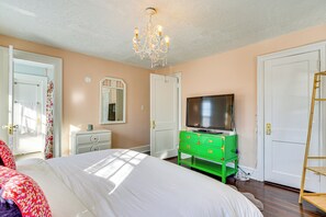 Une chambre à coucher avec un grand lit, une commode verte, un téléviseur et un lustre.