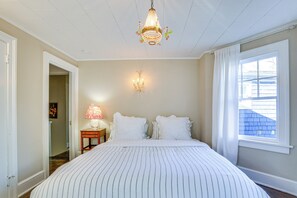 Un dormitorio con una cama grande, una araña, una l ámpara de pared, una ventana con cortinas y una puerta que da a otra habitación.
