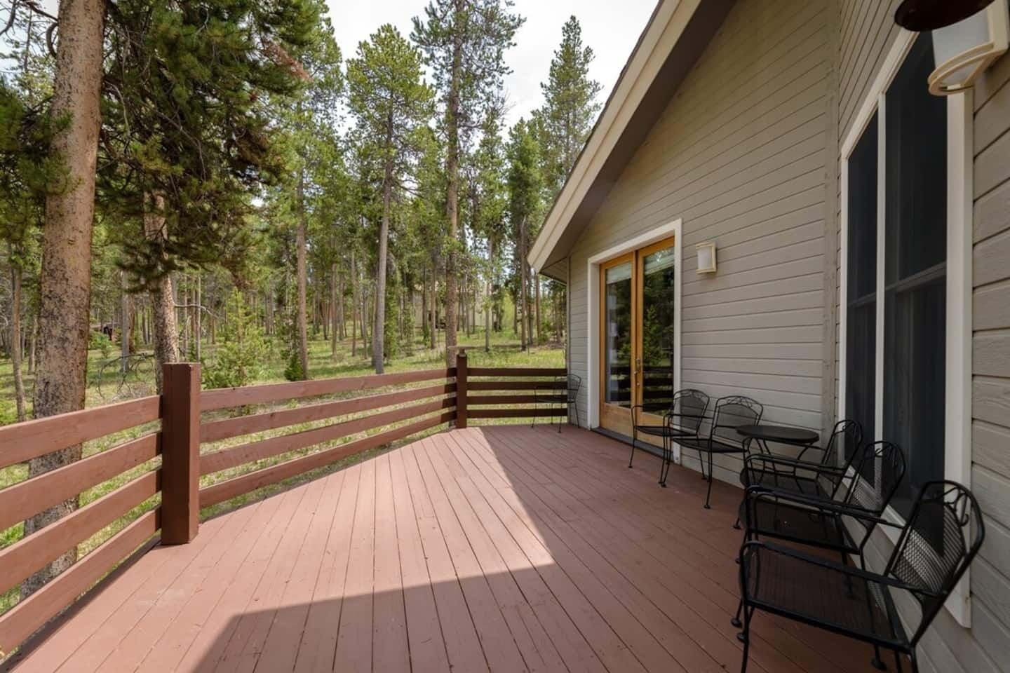 Une terrasse en bois avec des chaises et une table en métal, donnant sur une zone boisée.