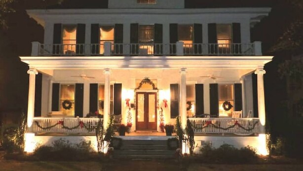 A two-story white building with a balcony, columns, and a front door.