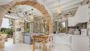 A rustic kitchen with stone walls, white cabinets, and a wooden dining table. - Zos Suites (Naxos)