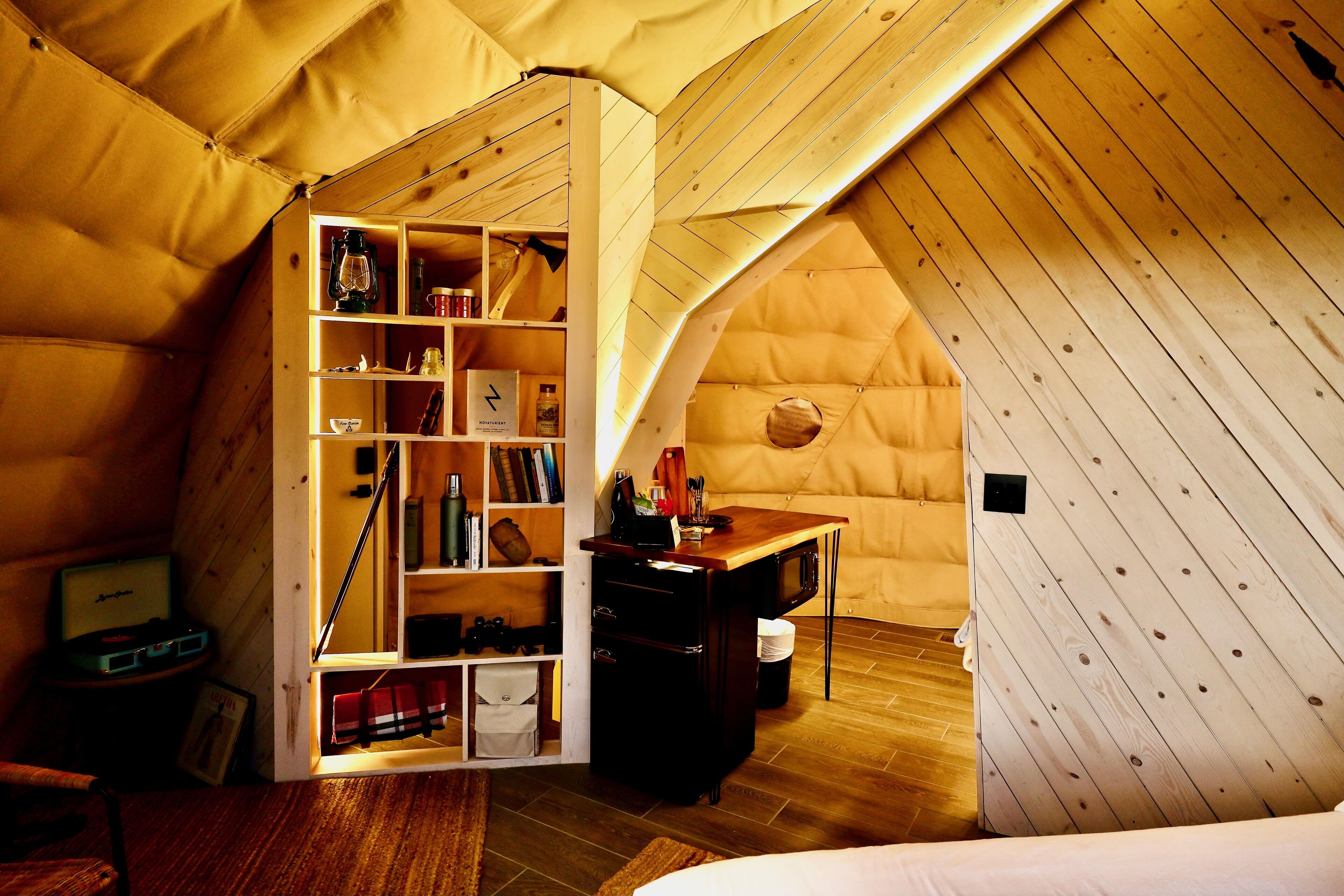 A cozy attic bedroom with a loft bed, wooden walls, a built-in bookshelf, and a small desk.