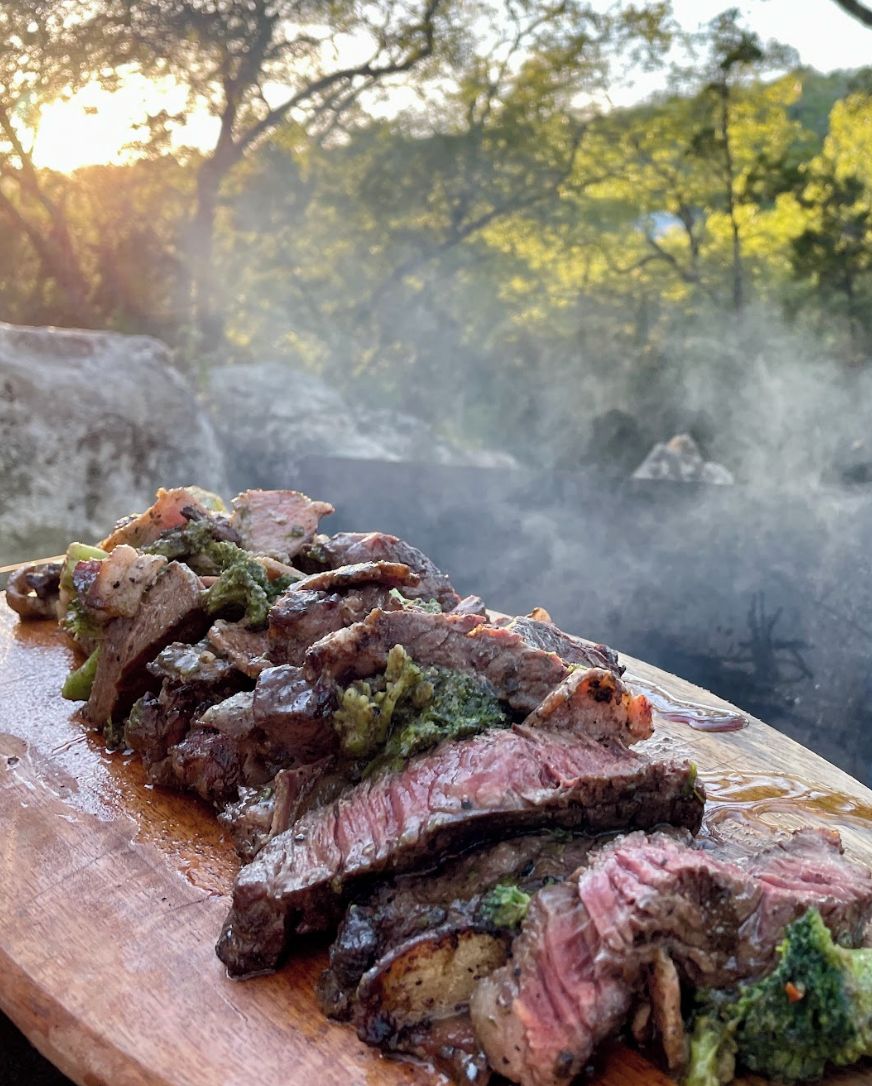 Une planche à découper en bois avec des tranches de steak et une sauce verte.