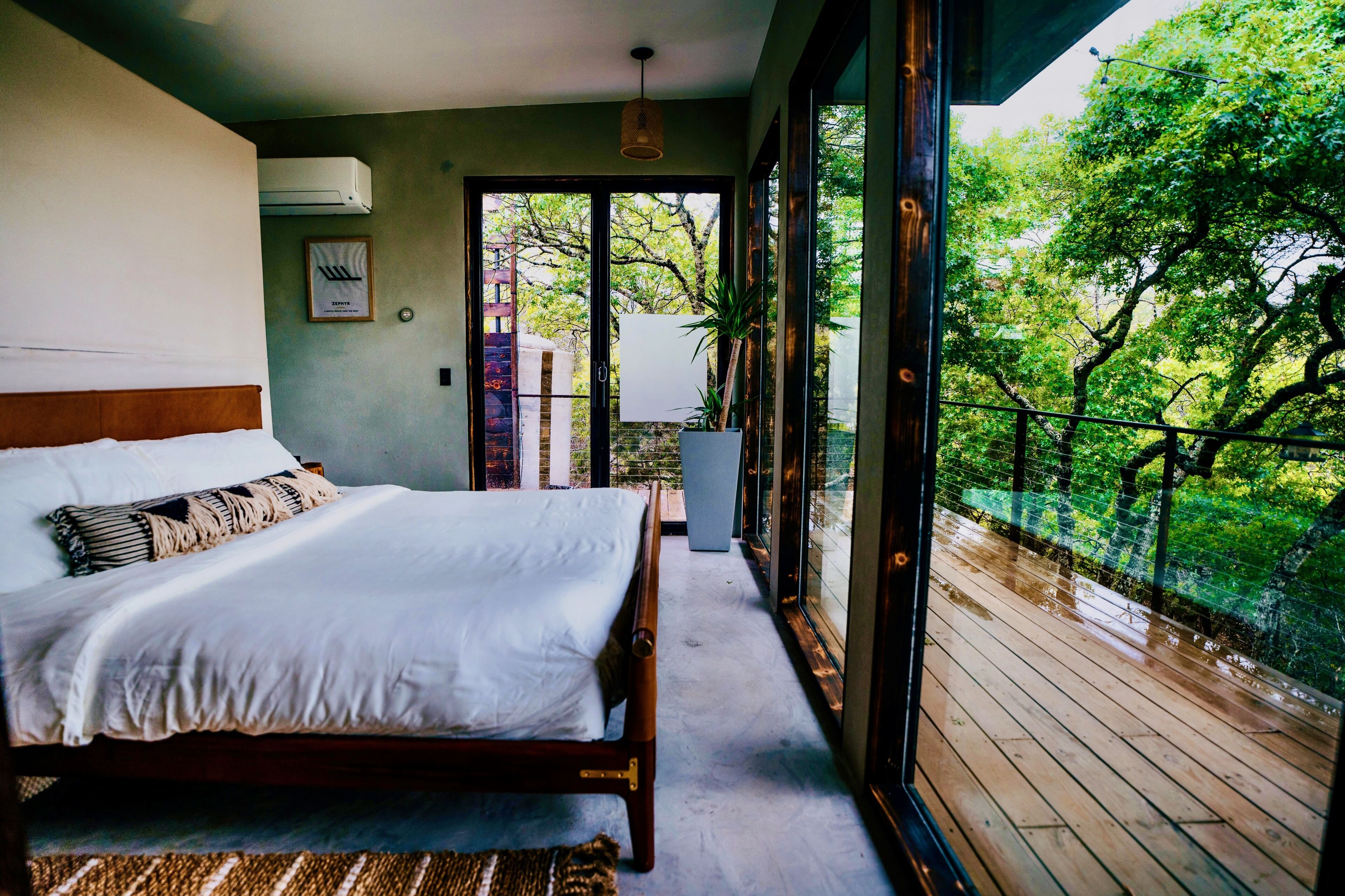 A bedroom with a bed, a potted plant, and a view of greenery outside.