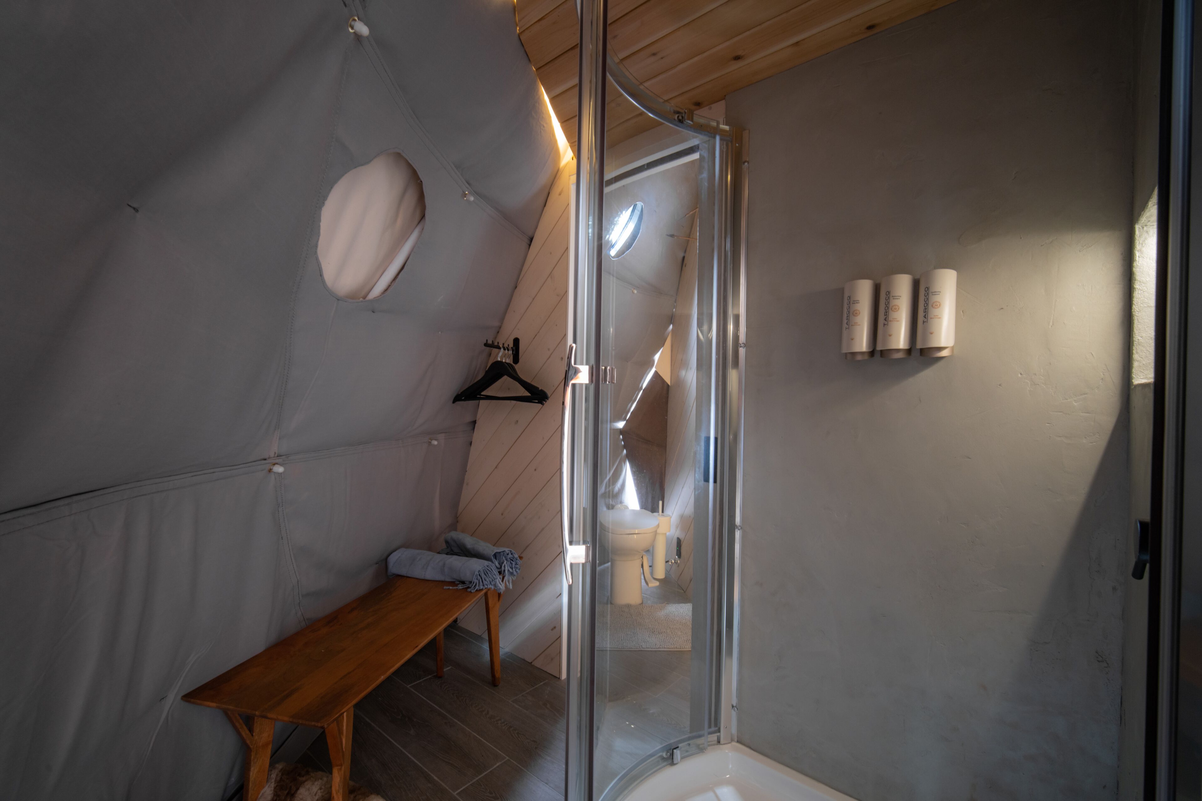 A compact, modern bathroom with a shower, toilet, and a bench.