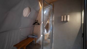 A compact, modern bathroom with a shower, toilet, and a bench.