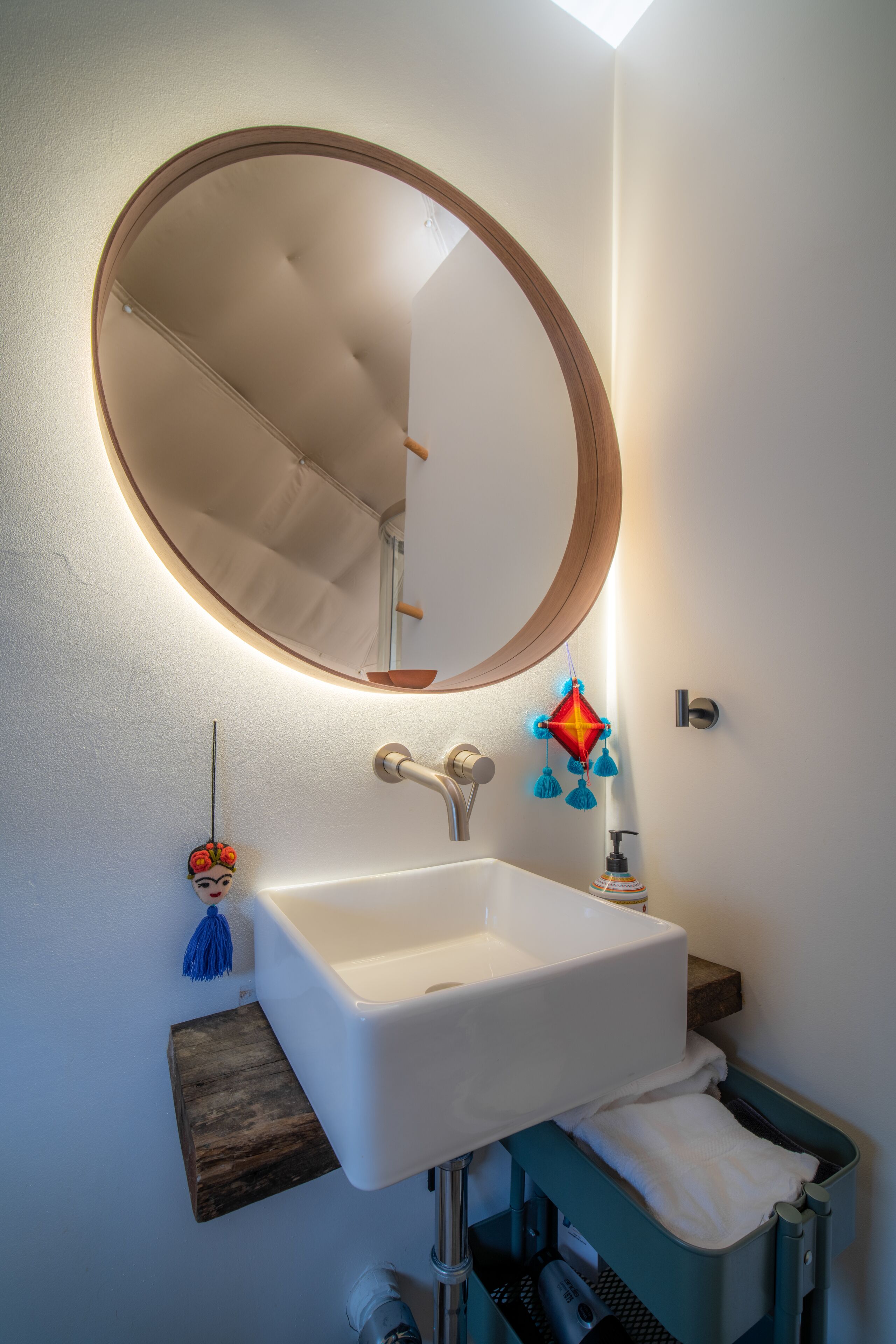 Un baño con un espejo redondo, lavamanos blanco y un perchero para toallas.