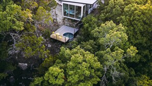 Una casa moderna amb façana de vidre, envoltada per un bosc dens.