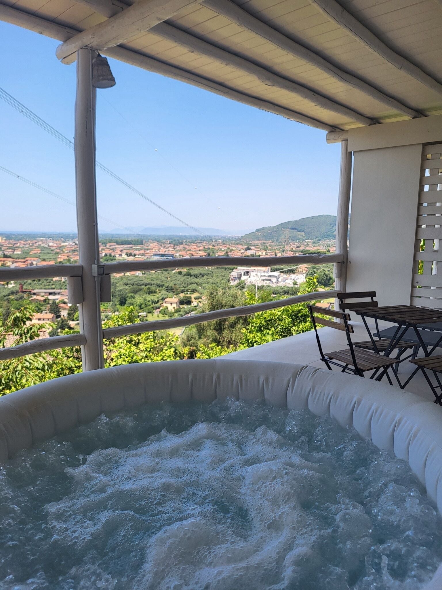 Uma banheira de hidromassagem numa varanda com vista para uma cidade e colinas.