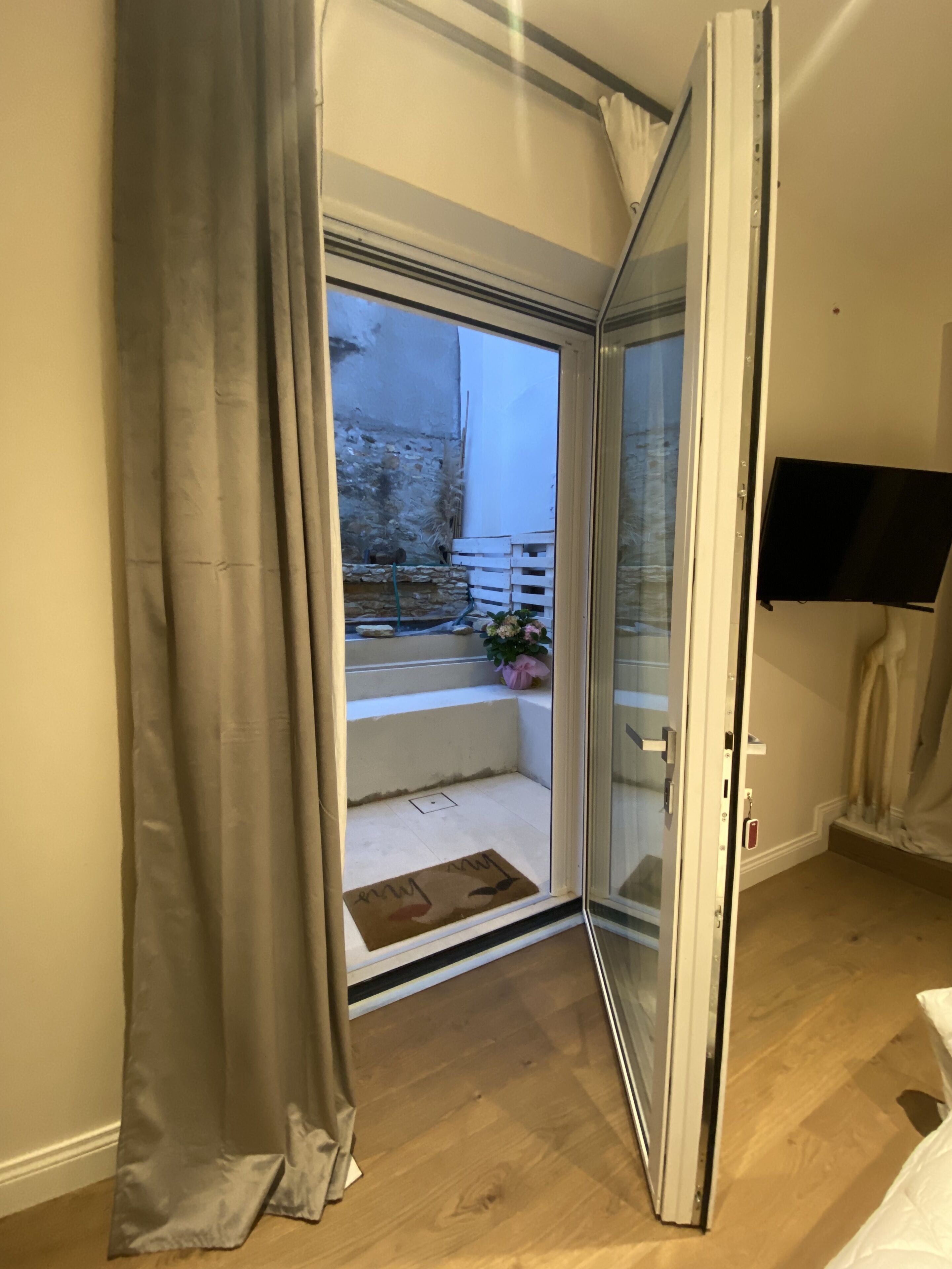 A room with a sliding glass door leading to a balcony with a stone wall and a small garden area.