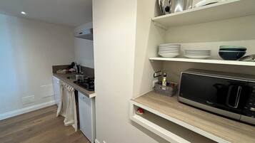 A compact kitchen with a microwave, stove, and shelves above holding dishes and a bottle.