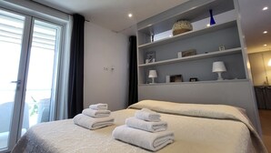 Een moderne hotelkamer met een groot bed, een inbouwkast met decoratieve objecten, en uitzicht op het buitengebied via een schuifdeur.