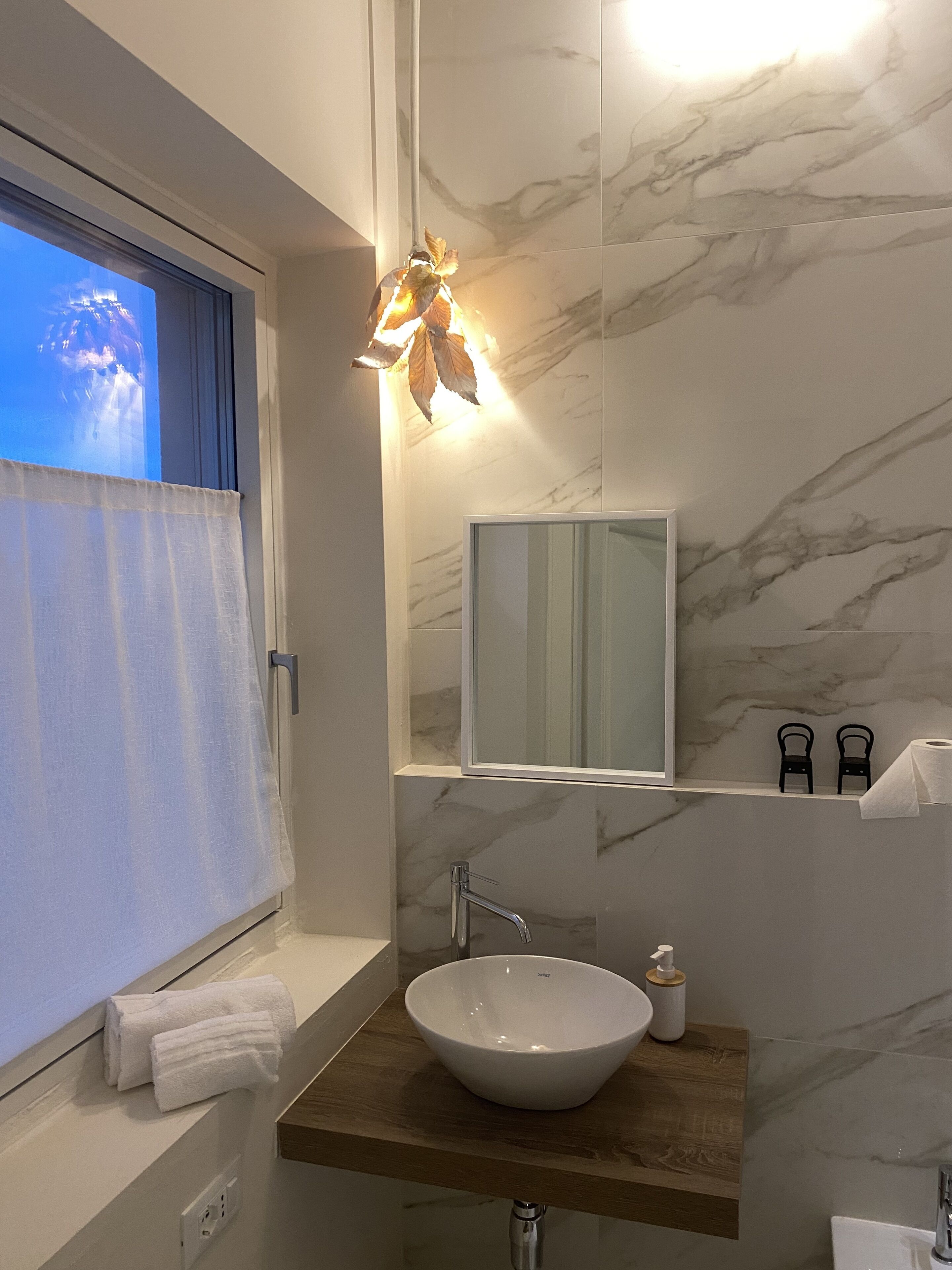 A modern bathroom with a marble backsplash, a large mirror, a vessel sink, and a window with a view.