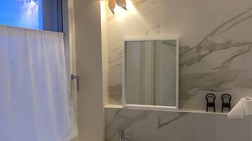 A modern bathroom with a marble backsplash, a large mirror, a vessel sink, and a window with a view.