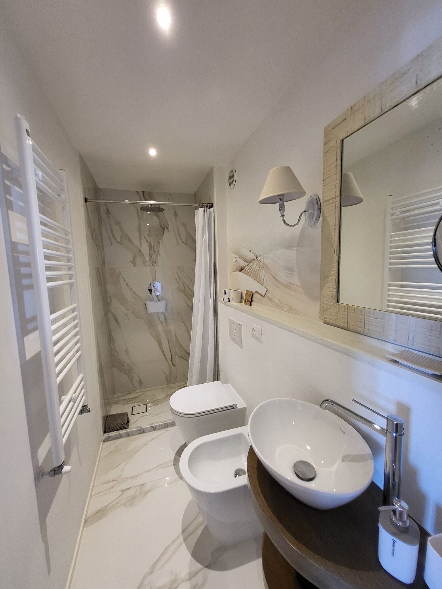 Un baño moderno con suelo de mármol, un lavabo blanco, un bidé, una ducha con puerta de cristal y un espejo grande.
