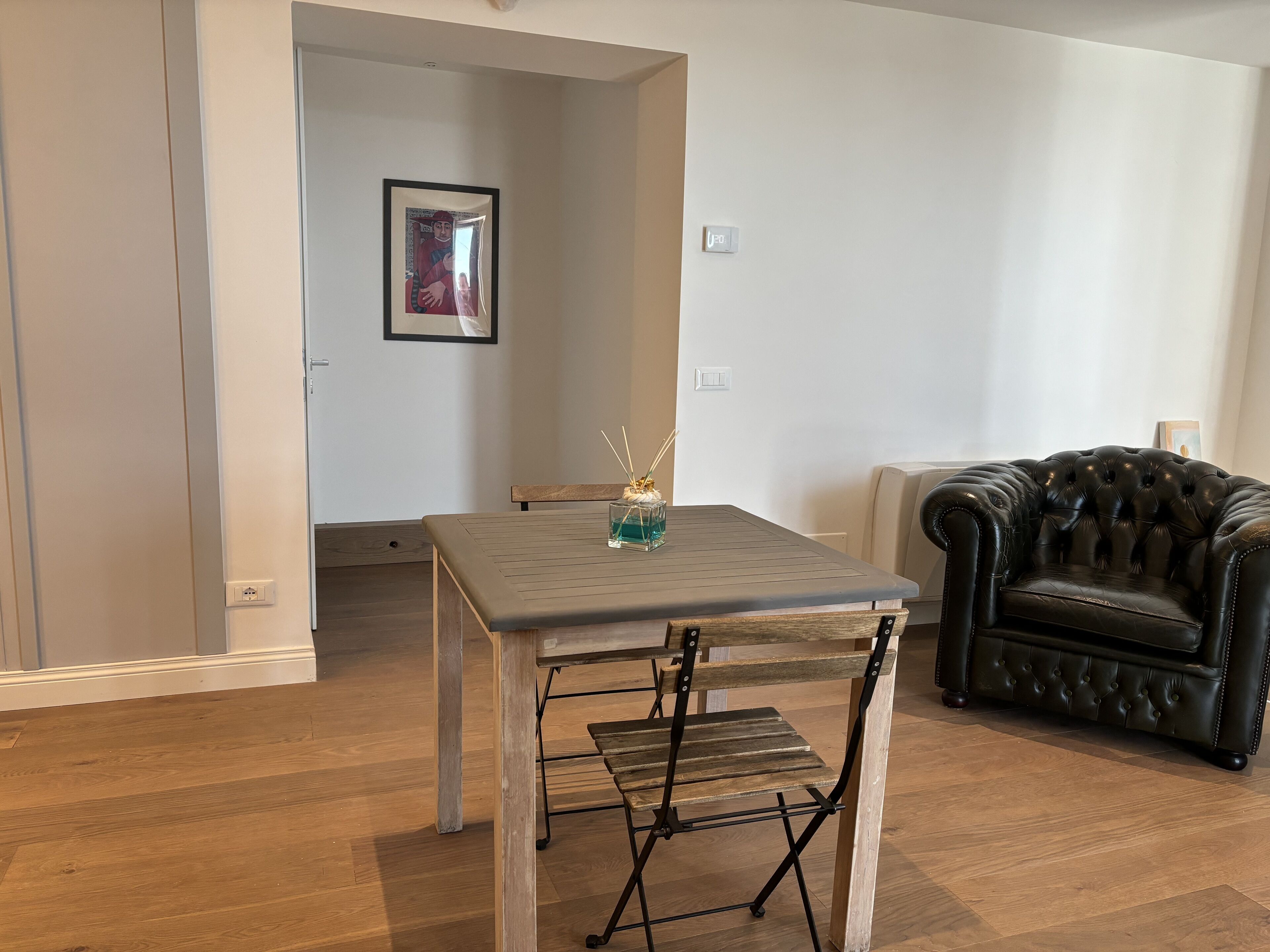 Una stanza con pavimento in legno, un tavolo con piano in vetro, una poltrona in pelle nera e un quadro appeso alla parete.