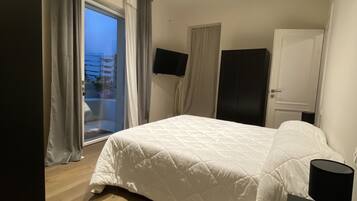 A bedroom with a bed, a desk, a TV, and a door.