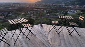 Een houten terras met tafels en stoelen, met uitzicht op een vallei met gebouwen en bergen in de verte.