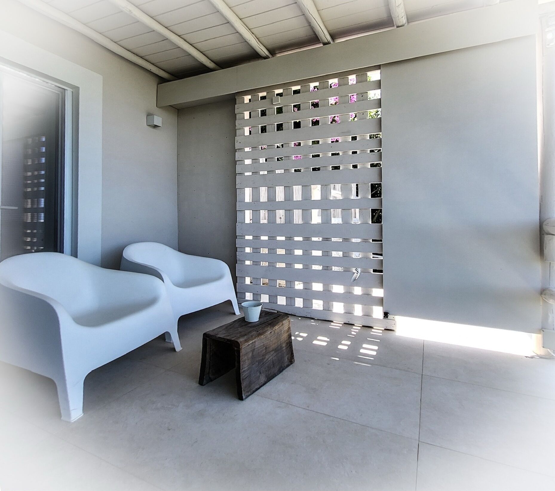 Un espace extérieur moderne aménagé avec deux chaises blanches et un banc en bois.