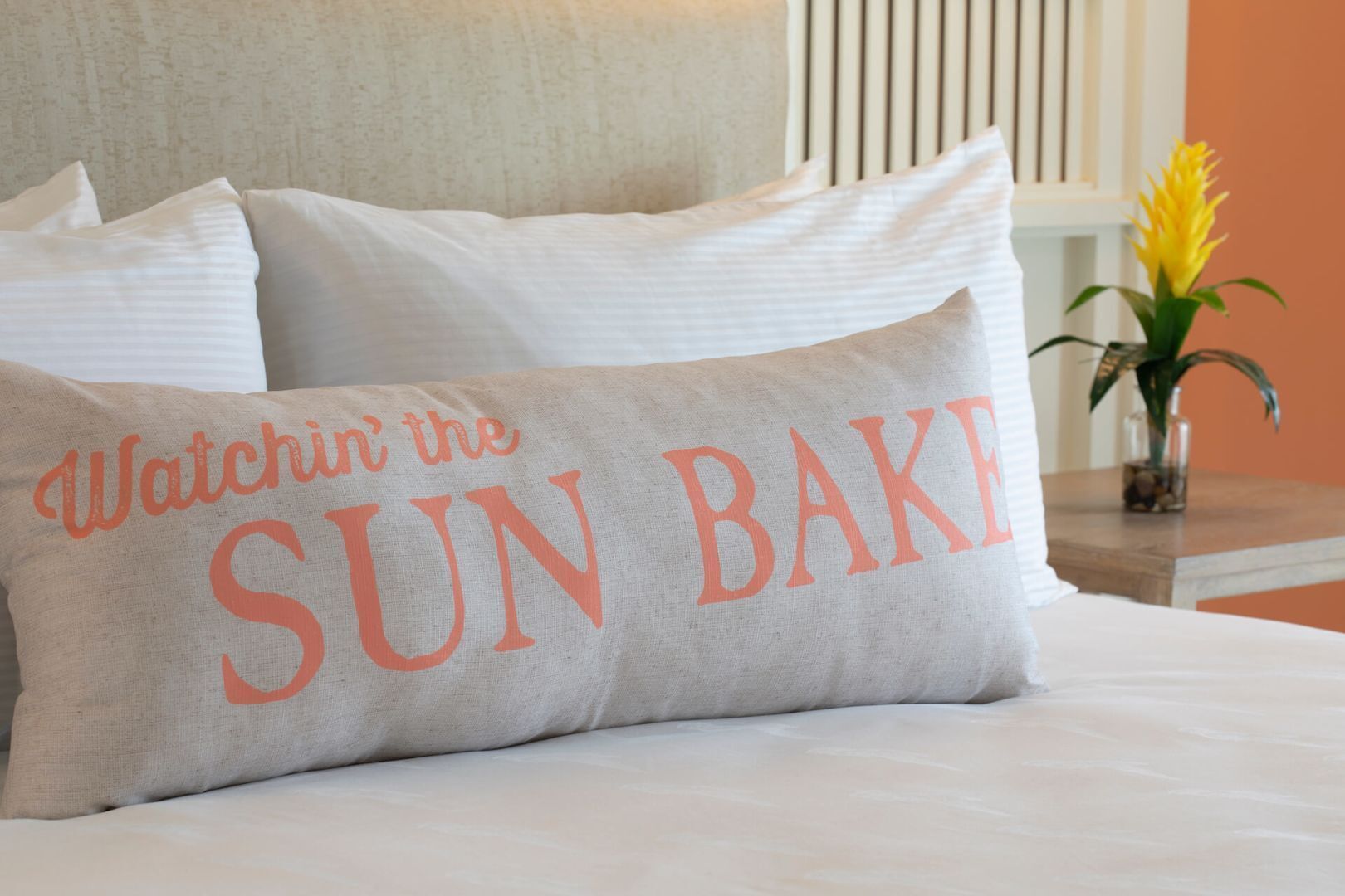 A bed with a pillow that reads "Watching the SUN BAKE".