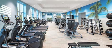 Une salle de sport moderne équipée de tapis de course, d’appareils de musculation et ornée d’une fresque murale représentant une scène de plage.