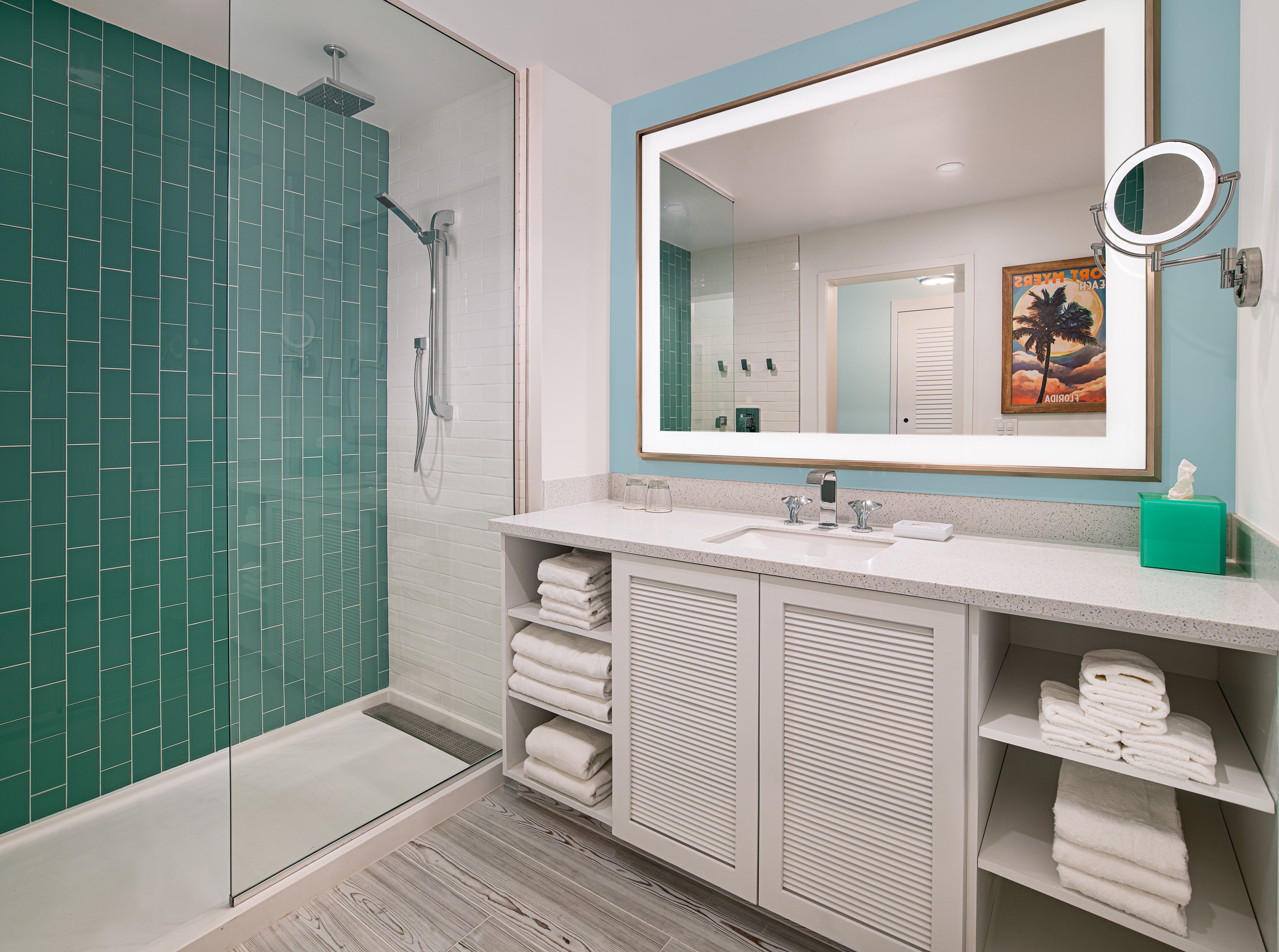 A modern bathroom with a glass shower enclosure, white tiled walls, and a large mirror with a round mirror above it.