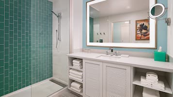 A modern bathroom with a glass shower enclosure, white tiled walls, and a large mirror with a round mirror above it.
