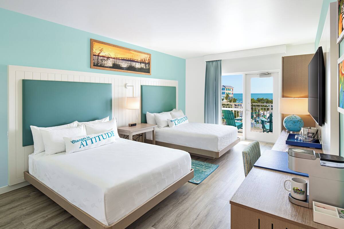 Une chambre d’hôtel avec deux lits, un bureau, une télévision et un balcon donnant sur l’océan.