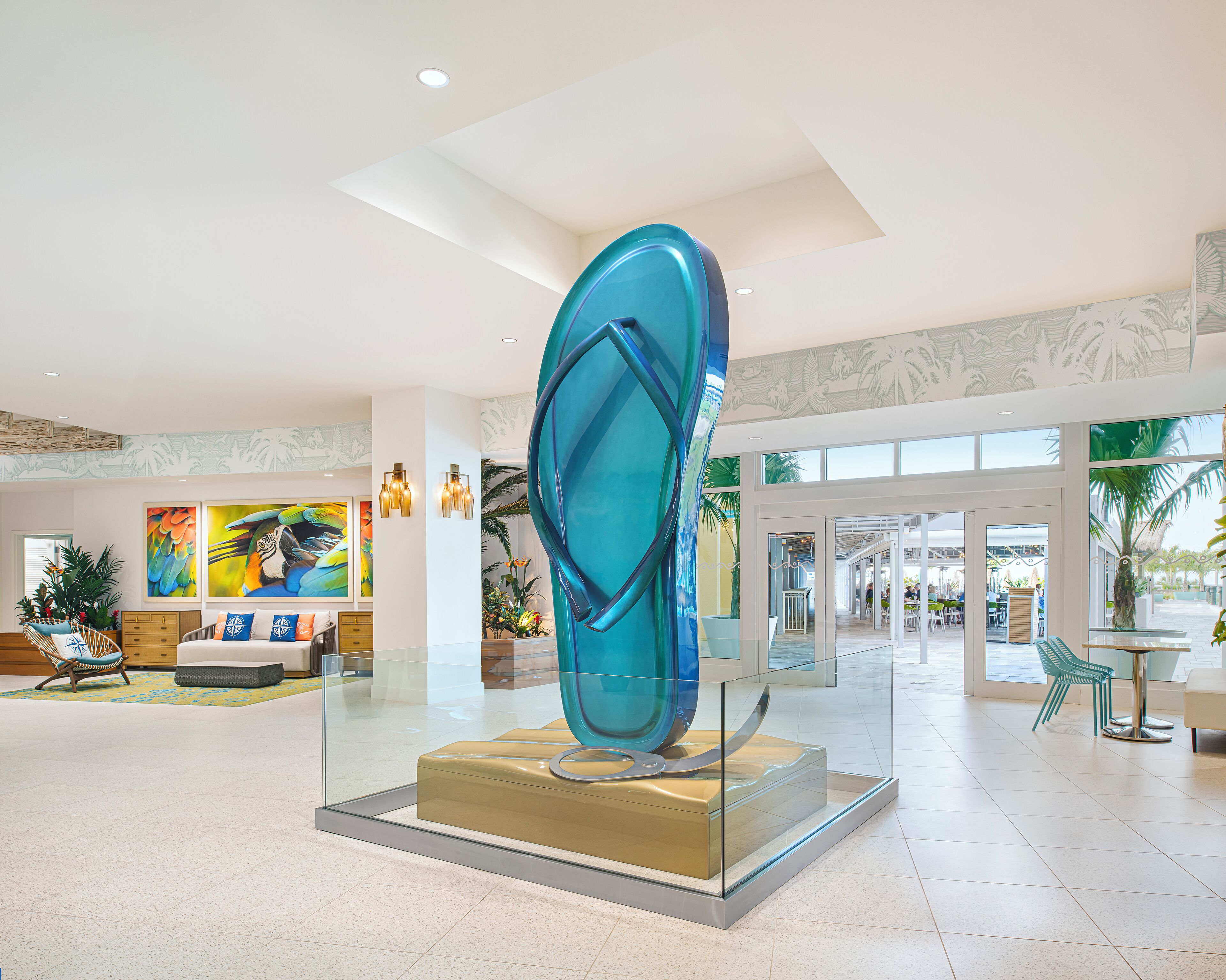 A modern lobby with a large glass sculpture, a seating area with a sofa and chairs, and a view of the outdoor area through large windows.