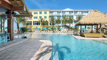 A resort pool area with a clear blue pool, lounge chairs, and a building with balconies in the background.