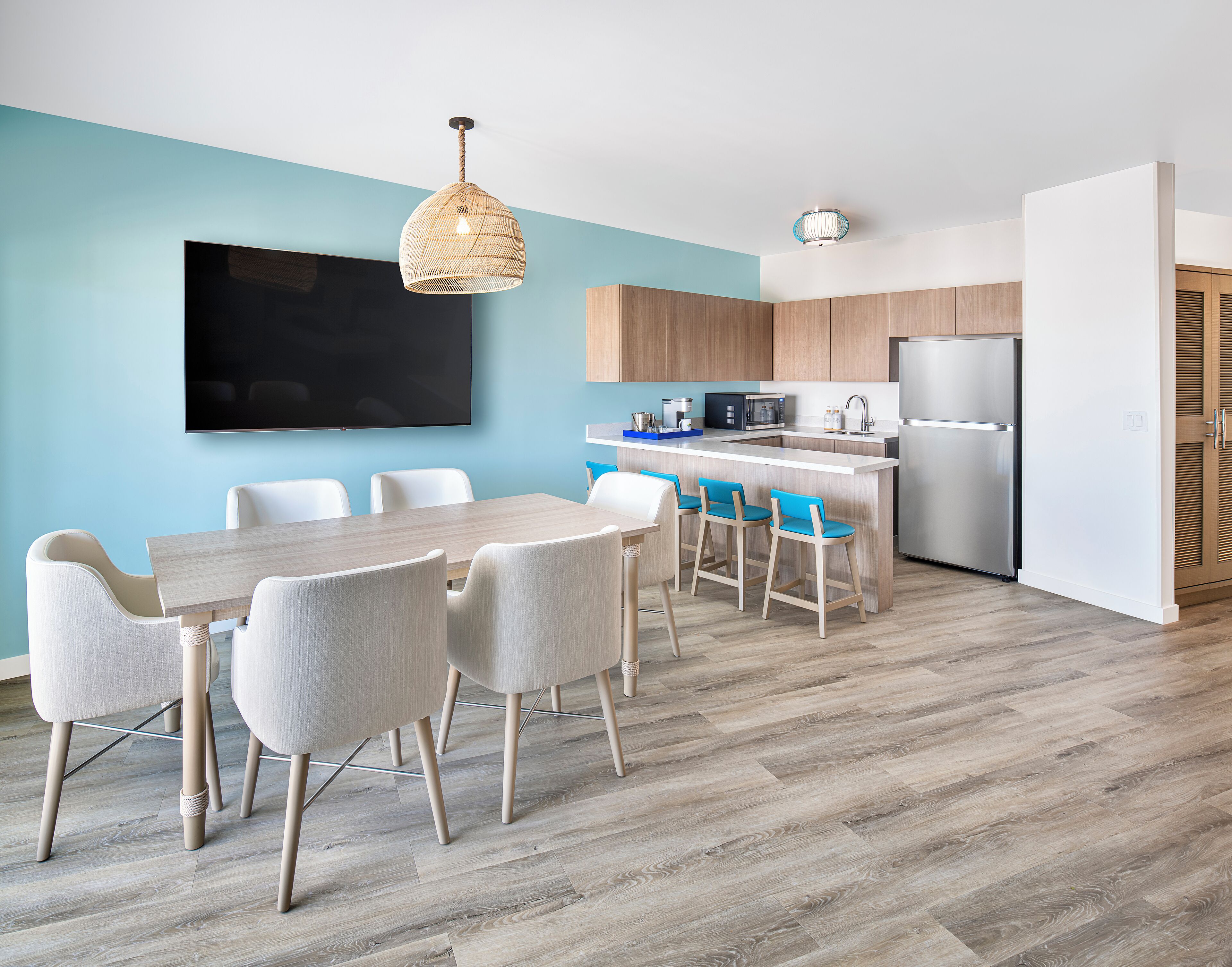 Une cuisine moderne dotée d’un îlot central, d’un coin repas avec une table et des chaises, et d’un grand téléviseur à écran plat fixé au mur.