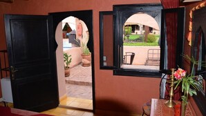 An open black door leading to a courtyard with potted plants and a view of a pool and outdoor seating. - Villa Tata Marie Marrakech (Marrakech-Safi)