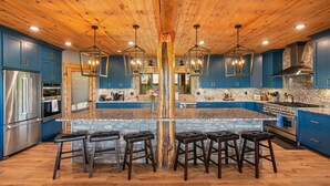 A spacious kitchen with blue cabinets, a large island with stools, and a wooden ceiling. - Luxe Log Cabin: Teton Views, Huge Patio, & Hot Tub (Tetonia)