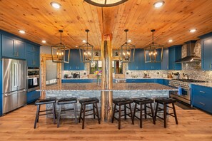 A spacious kitchen with blue cabinets, a large island with stools, and a wooden ceiling.