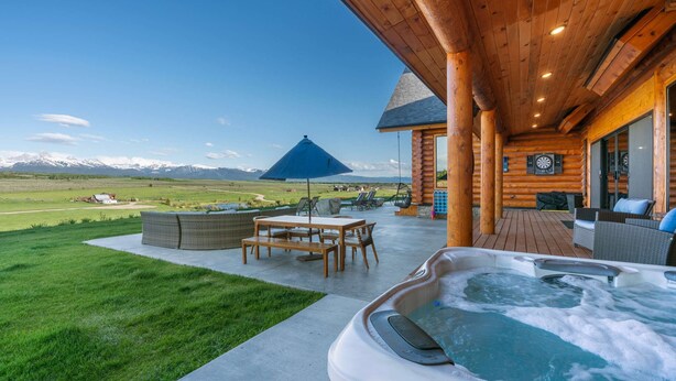 A wooden cabin with a hot tub, outdoor seating, and a mountain view. - Luxe Log Cabin: Teton Views, Huge Patio, & Hot Tub (Tetonia)